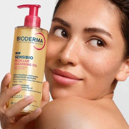 Model with radiant skin holding a bottle of the new 300ml size Sensibio Micellar Cleansing Oil